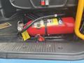 A red fire extinguisher mounted inside a vehicle with a yellow inspection tag and a black base with textured grip