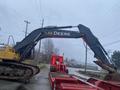 A yellow 2014 John Deere 350G excavator with a large black arm positioned above a red tractor on a loading ramp