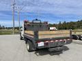 A 2010 Ford F-550 flatbed truck with a wooden bed and safety rails parked on a gravel surface, viewed from the rear