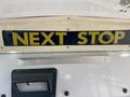 A sign on a vehicle that reads NEXT STOP in large yellow letters against a black background