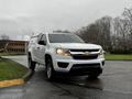 A white 2019 Chevrolet Colorado facing slightly to the right with headlights on and a truck cap in the bed