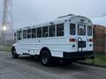 A 2016 International 4200 school bus with a white exterior features multiple windows and stop lights on the rear with a black ladder attached to the back