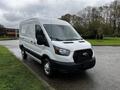 A white 2021 Ford Transit van parked with a front view showing large headlights a black grille and sliding side doors