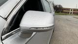 A silver 2013 Lincoln MKT with a raindrop-covered side mirror reflecting light