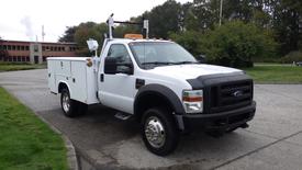 A white 2008 Ford F-450 Super Duty truck with an utility body and amber light on top