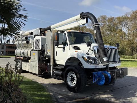 A 2013 International 7400 vacuum truck with a large hose mounted on the side and visible storage compartments for equipment and tools