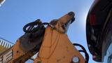 A close-up of the arm and hydraulic attachments of a 2015 Case 580 backhoe loader with a visible bucket and hose connections