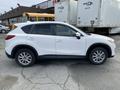 A white 2016 Mazda CX-5 SUV is parked, showing its side profile with five-spoke alloy wheels and tinted windows.