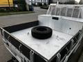 A 2014 Ford F-250 SD truck bed with a silver surface and a black tire placed in the center