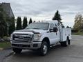 A white 2013 Ford F-350 Super Duty truck with a utility bed and orange roof lights parked on a concrete surface