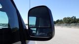 Side mirror of a 2012 GMC Savana showing a partial view of the vehicle's exterior and the road ahead