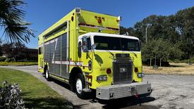 A bright yellow 1995 Freightliner FLL086 fire truck with a silver grille and reflective stripes is parked with its large compartment doors closed