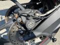 Close-up of a black brake caliper mounted on a motorcycle with visible brake rotor and chain components