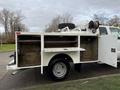 A white 2013 Ford F-350 SD with an open service bed showcasing storage compartments and a hose reel mounted on top