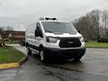 A white 2016 Ford Transit van with a black grille and front bumper parked on a road