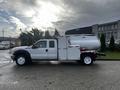 A white 2016 Ford F-550 with a utility body featuring a large tank and compartments on the side parked on a wet surface