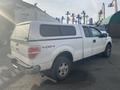 A white 2009 Ford F-150 truck with a camper shell on the bed and 4x4 badging on the side