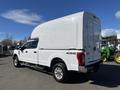 A white 2019 Ford F-350 SD with a high truck bed cover parked on a flat surface showcasing its four-wheel drive and large tires