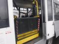 A yellow wheelchair lift inside a 2016 Chevrolet Express van with a metal mesh safety enclosure and red and white striped markings