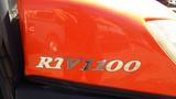 Close-up of the orange side panel of a 2013 Kubota RTV 1100 with the model name RTV1100 prominently displayed in silver letters