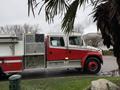 A red and silver 2001 Freightliner FL80 fire truck with a large water tank and emergency equipment visible on its side