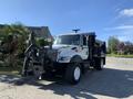 A 2007 International 7300 truck with a black dump body and snowplow attachment in front headlights on and parked on a driveway