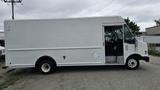 A white 2006 Ford Econoline with a large cargo area and a driver's side door open, parked on gravel