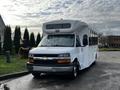 A white 2015 Chevrolet Express with large windows and a raised roof, designed for passenger transport, parked on a surface with a clean finish