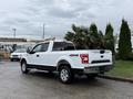 A white 2018 Ford F-150 pickup truck with a black stripe, equipped with a 4x4 feature, parked at a location with palm trees nearby