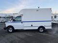 A white 2009 GMC Savana with a blue stripe on the side features a high-top cargo area and chrome wheels parked on a lot