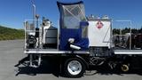 A 2006 Ford LCF 550 truck with a blue protective cover and various equipment mounted on the flatbed including tanks and machinery