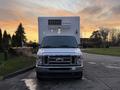 A 2021 Ford Econoline van with a white box refrigeration unit on the back positioned head-on in the foreground