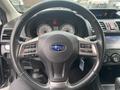 A steering wheel of a 2014 Subaru Impreza with buttons for audio control and phone functions, featuring a Subaru logo at the center and instrument dials visible behind it