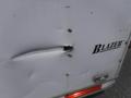 A damaged section of a 2010 Forest River Enclosed trailer showing a large dent and a small hole with the word Blazer visible