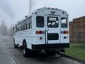 A 2016 International 4200 bus with a white exterior and large windows parked on the street