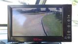 A monitor displaying a rearview camera feed showing a curved road ahead with grass on the side