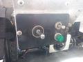 A control panel featuring various switches and indicators including a round dial, two toggle switches, and a green light indicator attached to a metallic surface