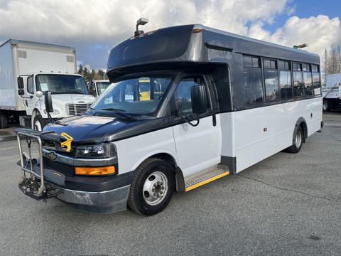 A 2018 Chevrolet Express shuttle bus with a black front, white body, and a metal guard on the front bumper