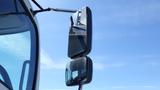 A side view mirror of a 2009 Hino 268 truck with a chrome finish and a black frame reflecting the sky