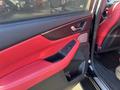 The interior door panel of a 2023 Acura MDX featuring red leather accents and a black handle