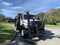 A 2007 International 7300 truck equipped with a front attachment and a rear loading area designed for waste collection or street maintenance