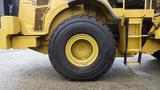 A close-up view of the tire of a 2019 Caterpillar 972M XE machinery featuring a black Michelin tire with a yellow rim and the Caterpillar logo