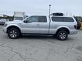 A silver 2014 Ford F-150 pickup truck with a cab cover and chrome wheels parked on a concrete surface