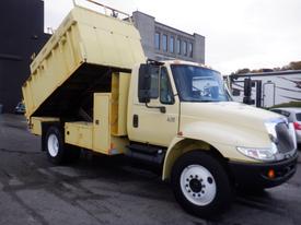 A yellow 2006 International 4200 truck with a dump bed and side loading compartment parked on a driveway