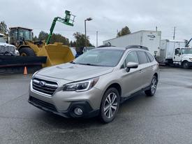 A 2019 Subaru Outback parked at a facility with a light beige exterior and modern design featuring a roof rack and alloy wheels