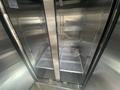 Interior view of a stainless steel food truck fridge with shelves and a wire rack interior