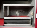 A metal storage compartment with two shelves and a red carpet lining within a truck cabinet