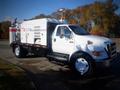 A white 2006 Ford F-650 utility truck with a large storage compartment and various equipment attached to the truck bed