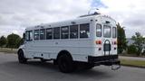 A white 2015 International PC105 bus with black wheels and a step at the back, featuring multiple windows and no markings on the side