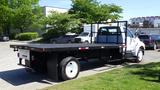 A white 2006 Ford F-650 flatbed truck with a black flatbed and a metal mesh headboard parked on a curb